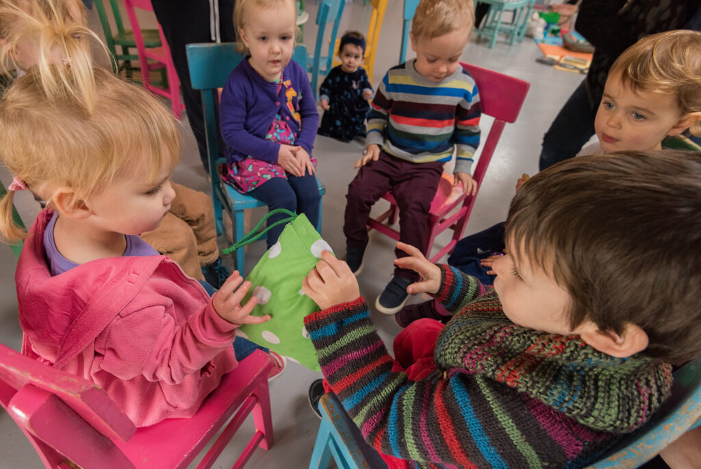 Children sat on chairs in a circle playing pass the parcel with reusable bags