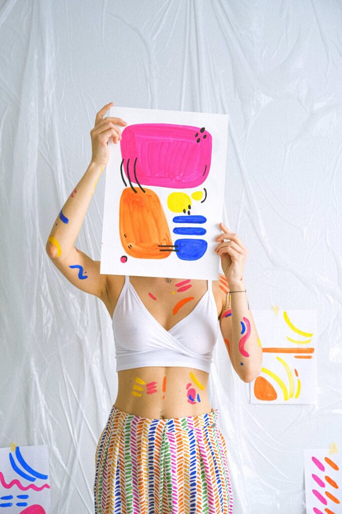 A woman holding up a colourful painting in front of her face