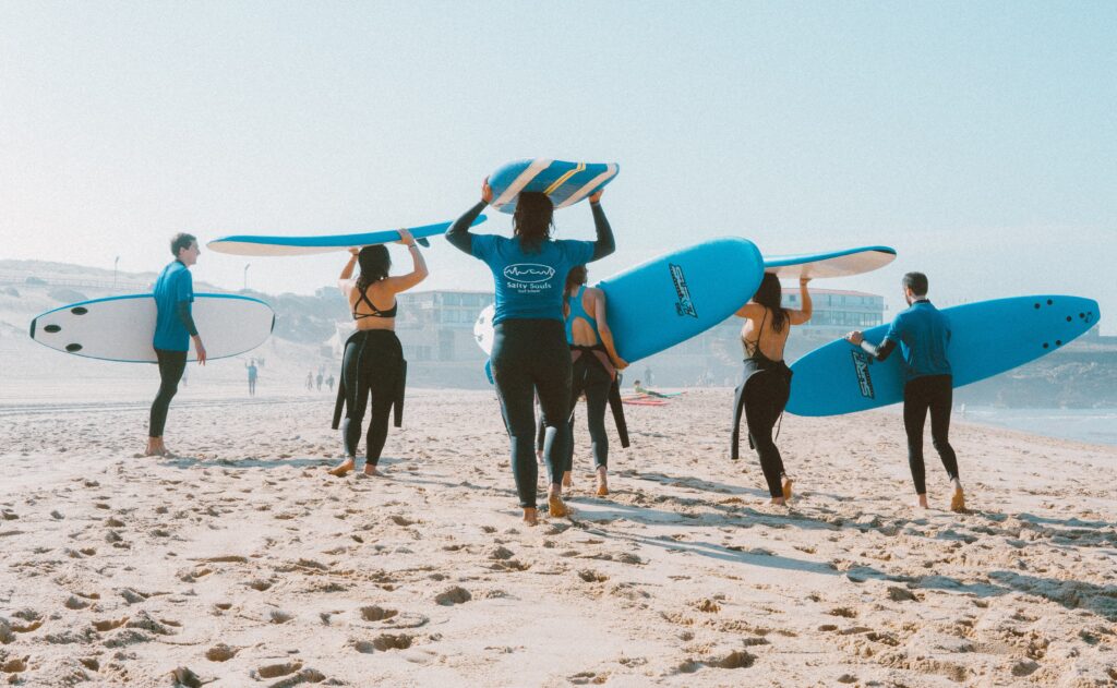 People carrying surf boards on the beach - teenage birthday party ideas