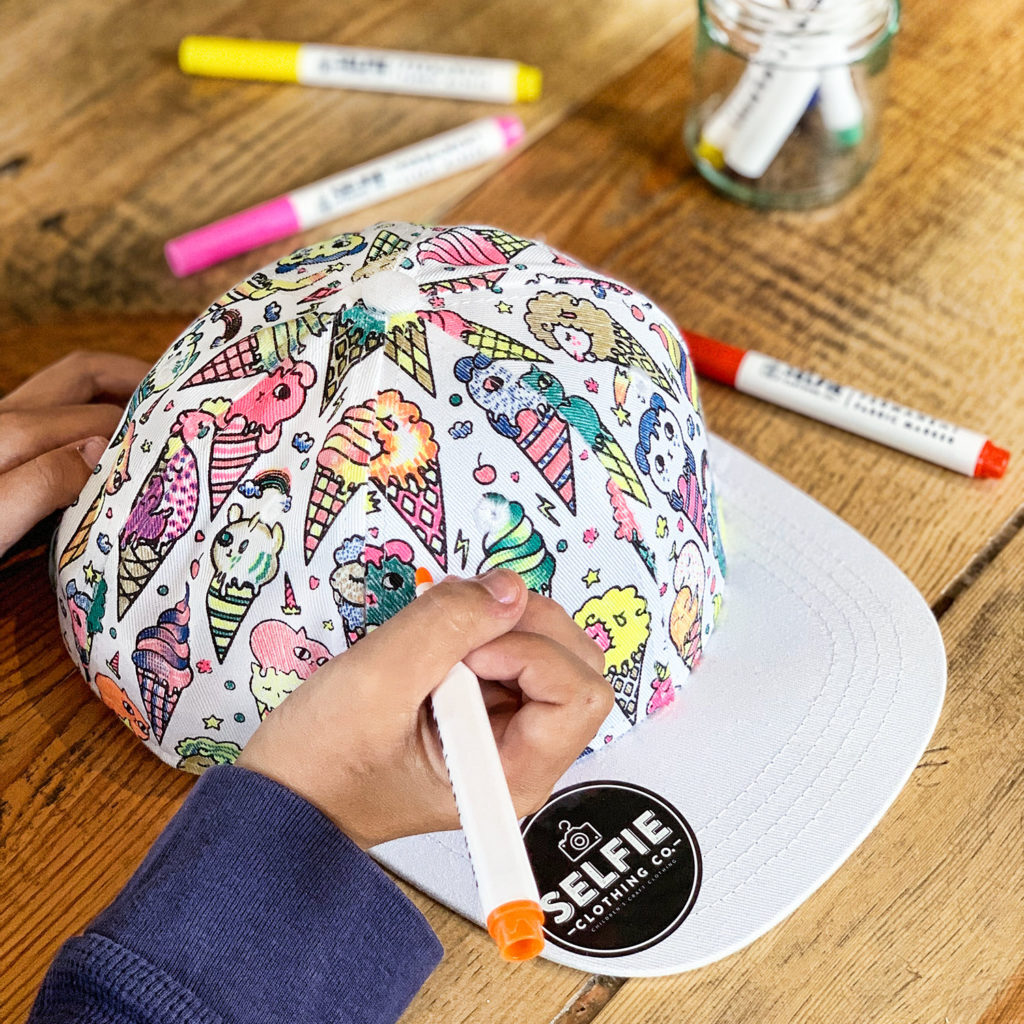 Child decorating a cap with pens