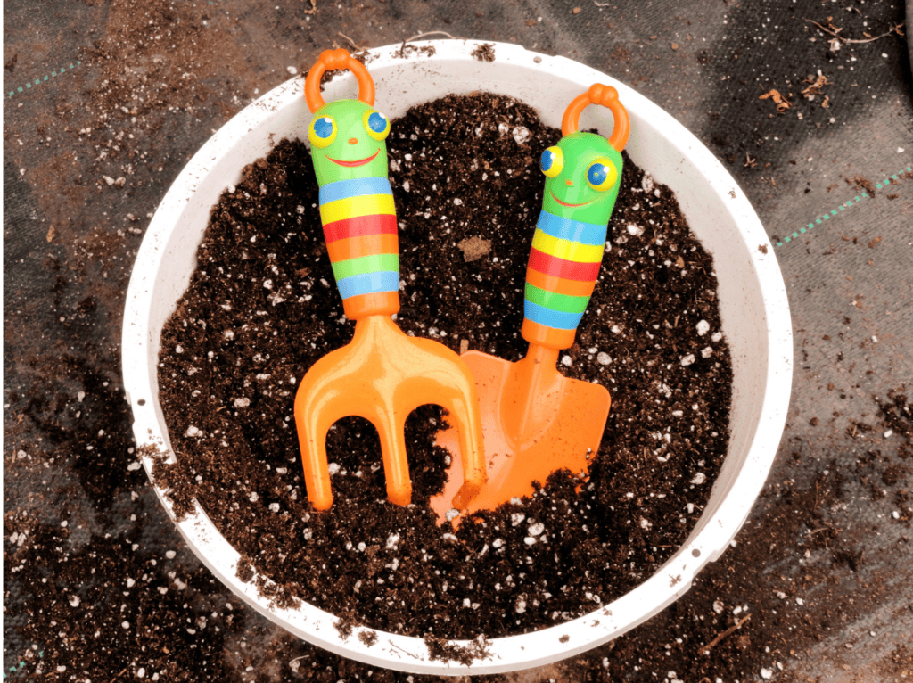 Orange kids gardening tools in a plant pot of dirt