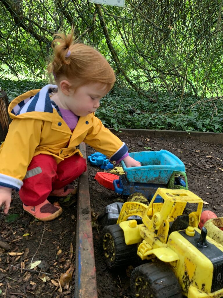 Lily playing with toy trucks - Forest school style parties