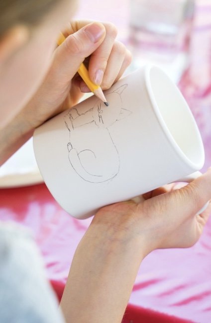 Someone drawing a cat on a mug
